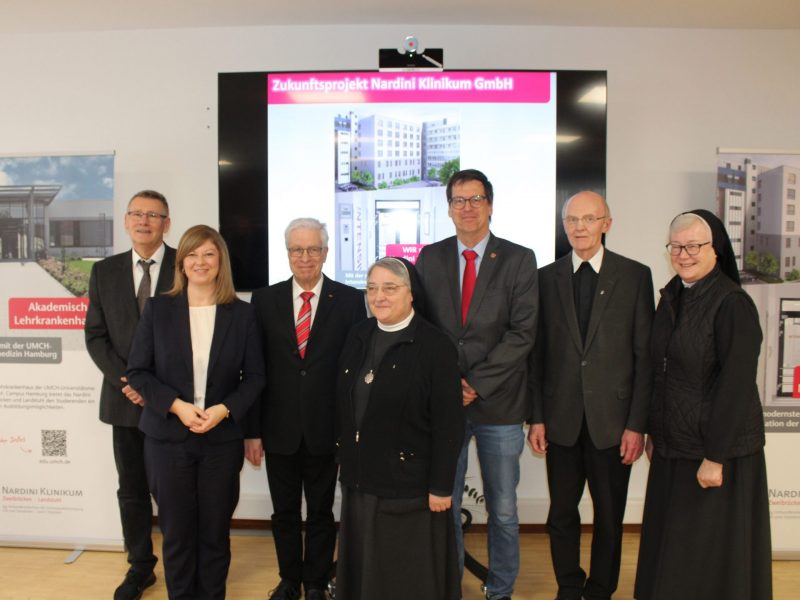 Eine Gruppe von sieben Personen, darunter Klinikvertreter und Ordensschwestern, steht vor einer Präsentation des Zukunftsprojekts der Intensivstation am Nardini Klinikum.