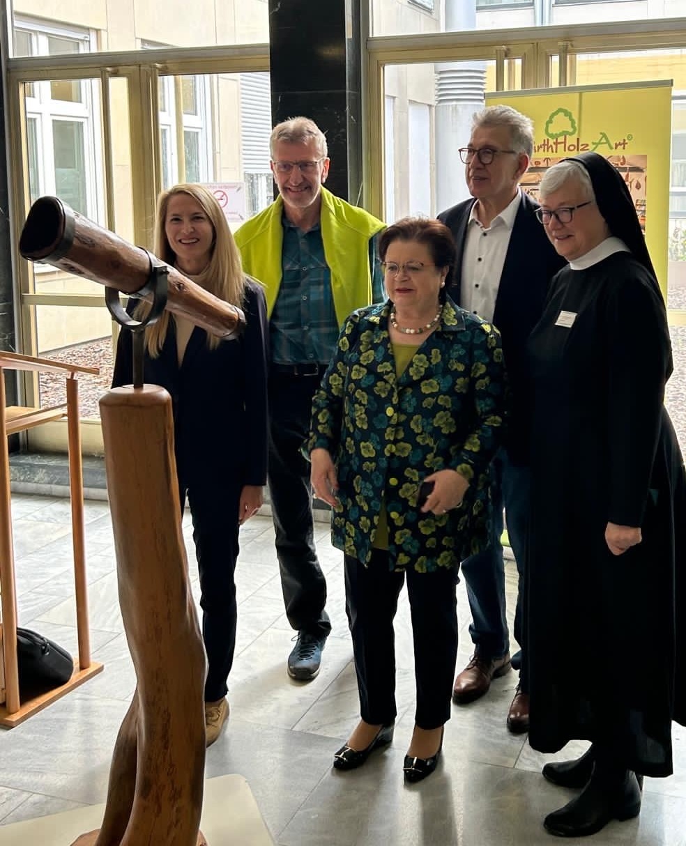Fünf Personen stehen vor einer Holzskulptur in der Eingangshalle des Nardini Klinikums in Landstuhl.