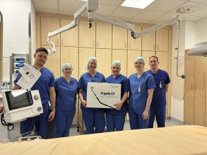 Sechs medizinische Fachkräfte in blauen OP-Kitteln stehen im Nardini Klinikum Landstuhl und halten ein Impella CP-Gerät.